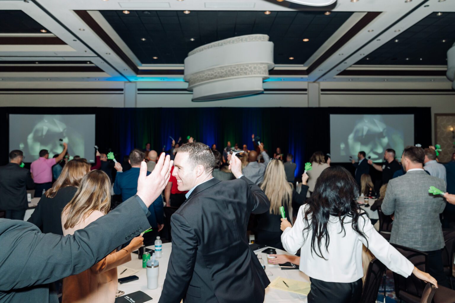 Sales reps on their feet cheering and waving green hand clappers during a general session in a hotel ballroom