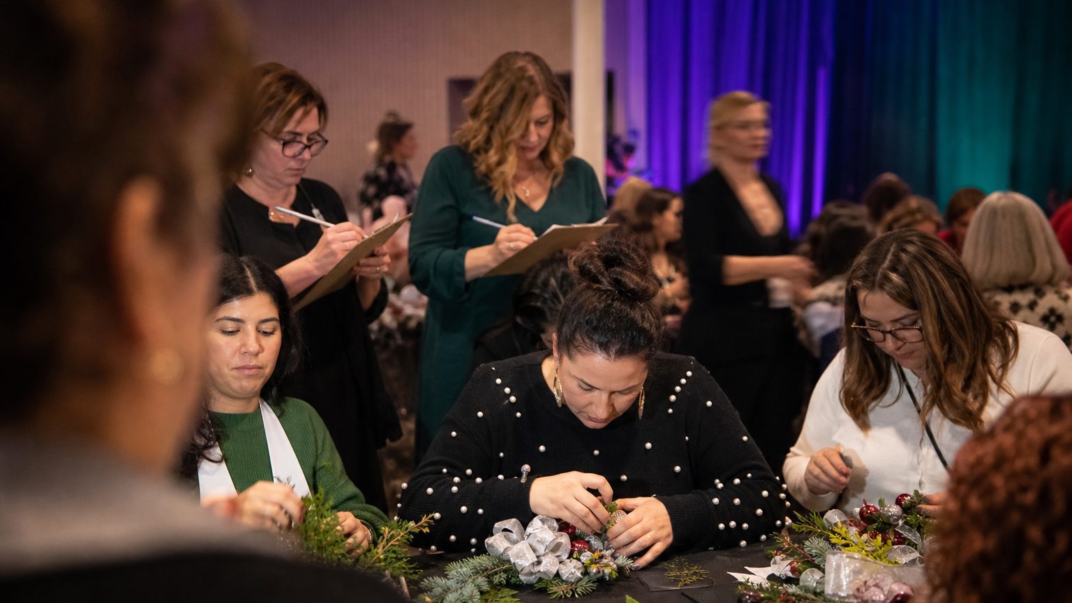 Several participants seated at a table, intensely assembling and decorating holiday-themed crafts with colorful materi