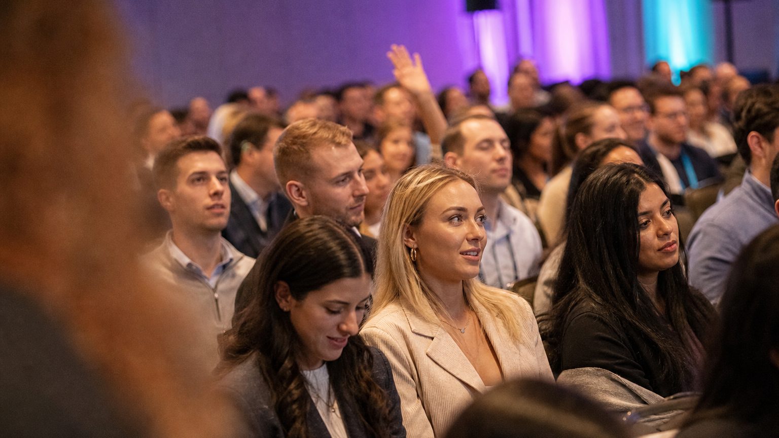 A presenter gesturing at the front of a packed ballroom
