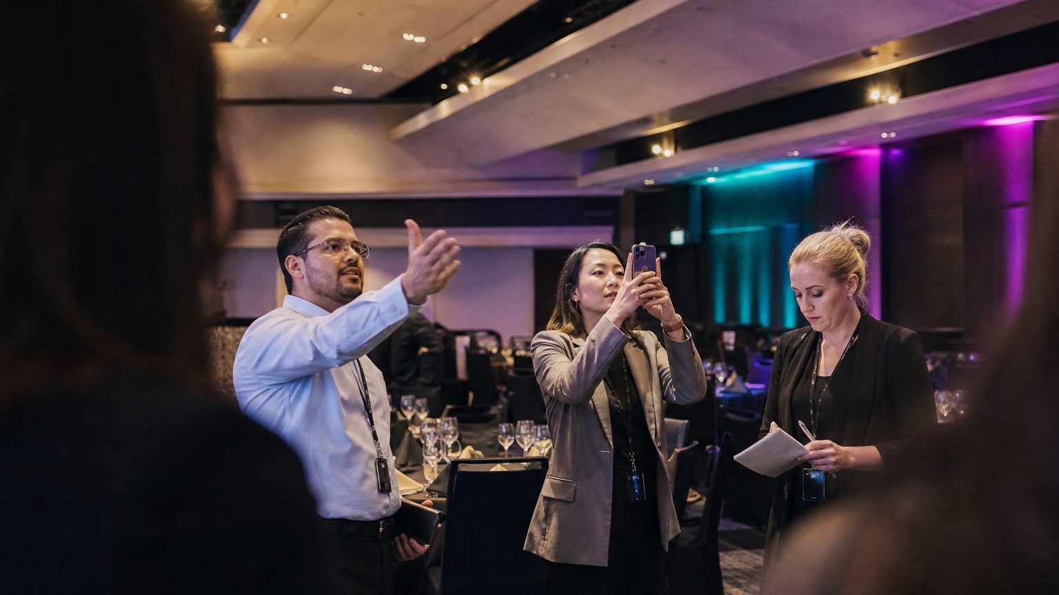 A venue manager gesturing across a function space to two corporate planners