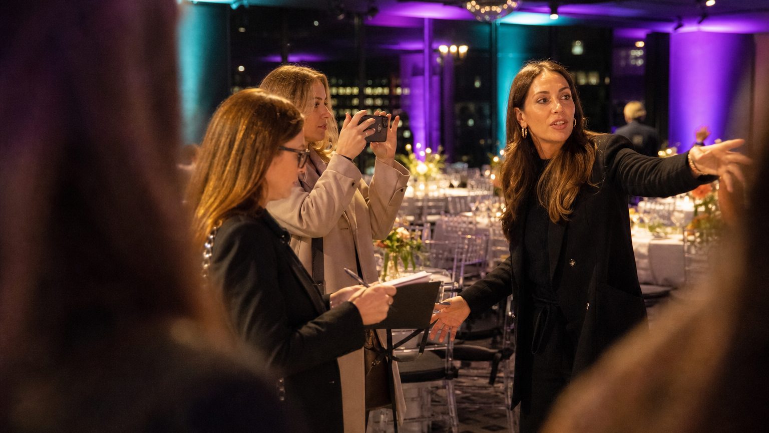 A venue manager gesturing across a function space to two corporate planners