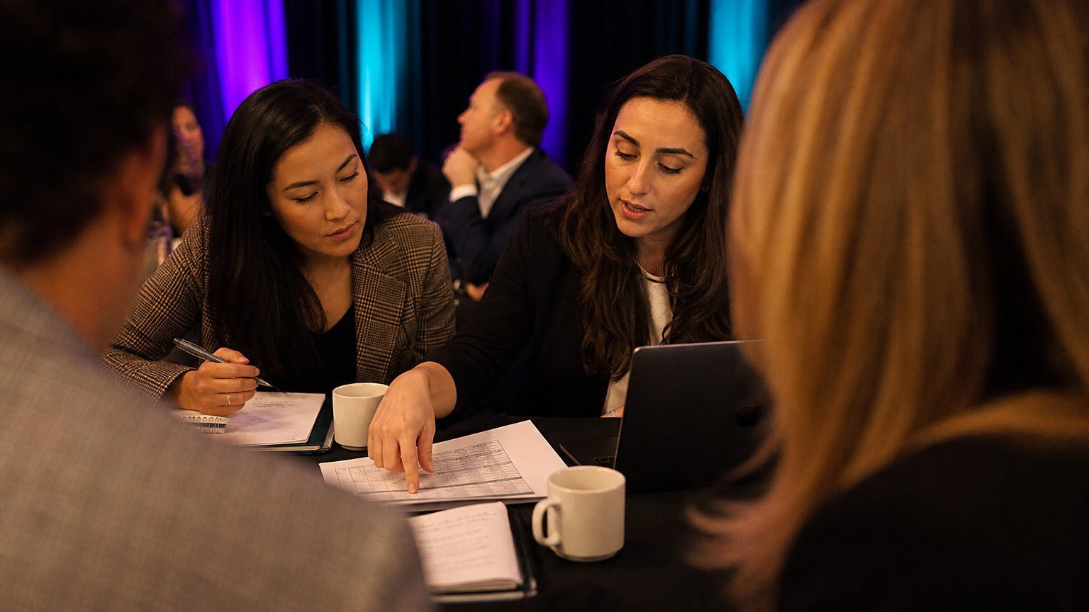 Two corporate event planners across a hotel meeting-room table mid-discussion