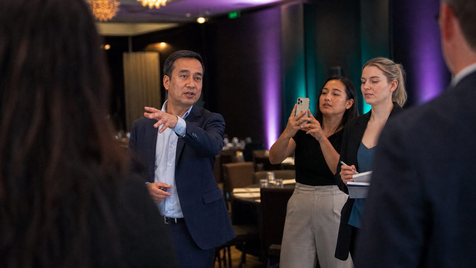 A venue manager gesturing across a function space to two corporate planners