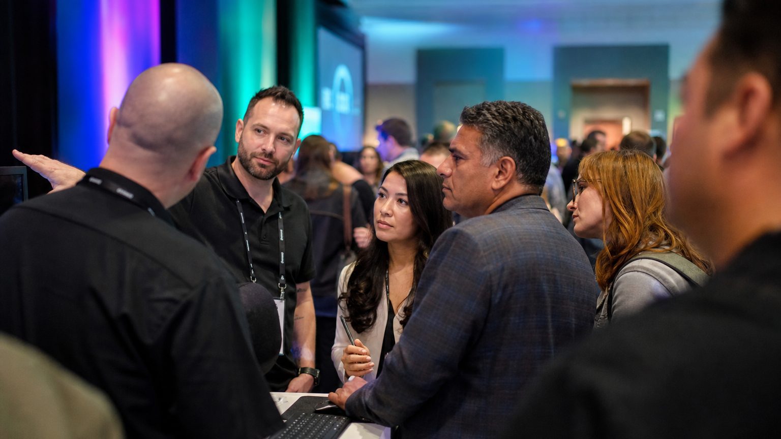 Two exhibitors in branded polos talking with three visitors at a booth counter