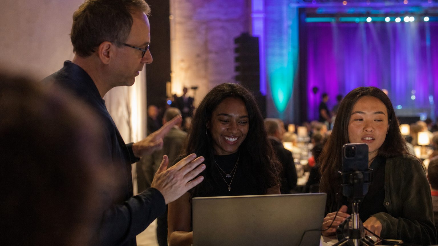 Three colleagues around a laptop and a phone on a stand