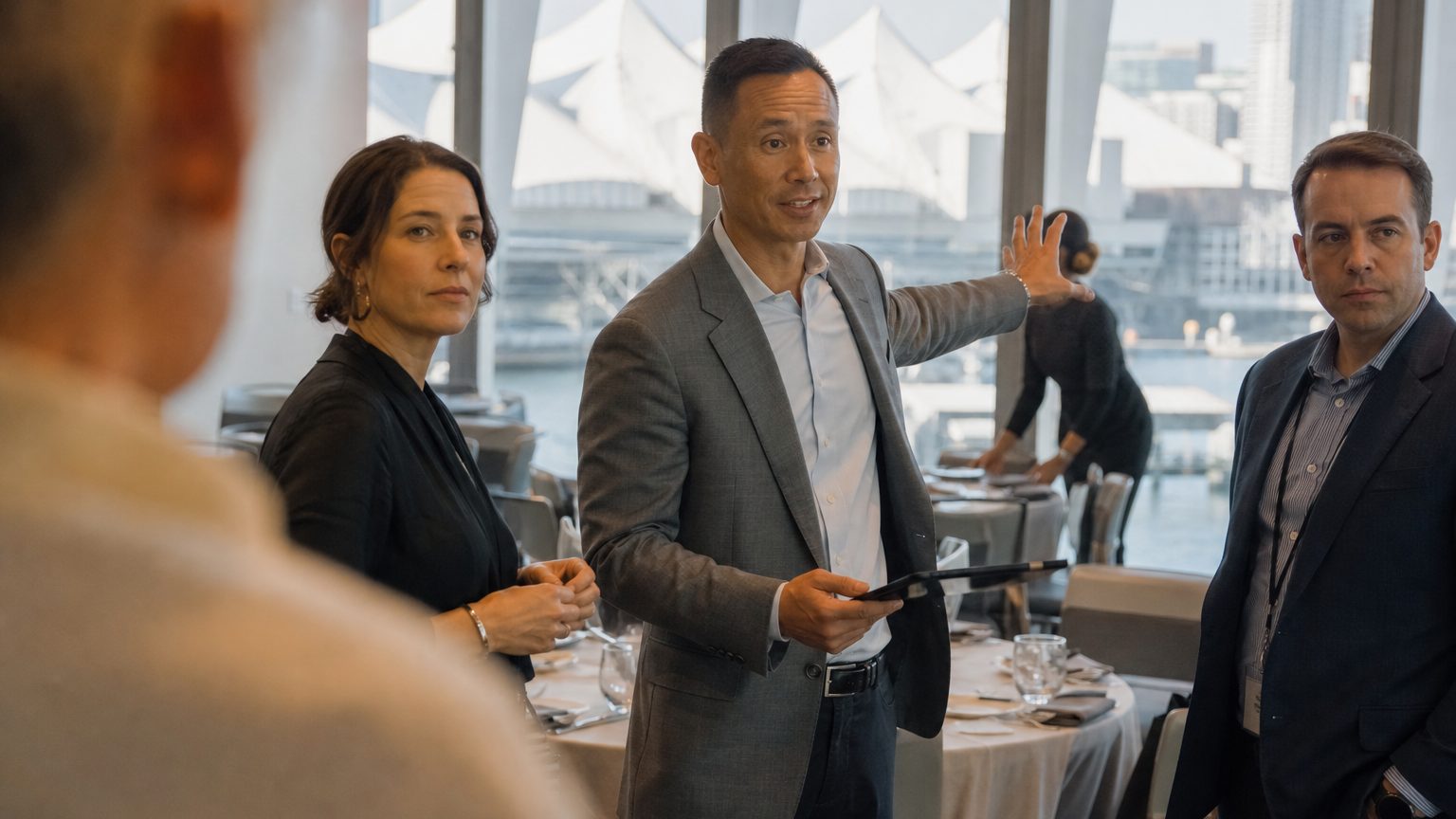 A venue manager gesturing across a function space to two corporate planners