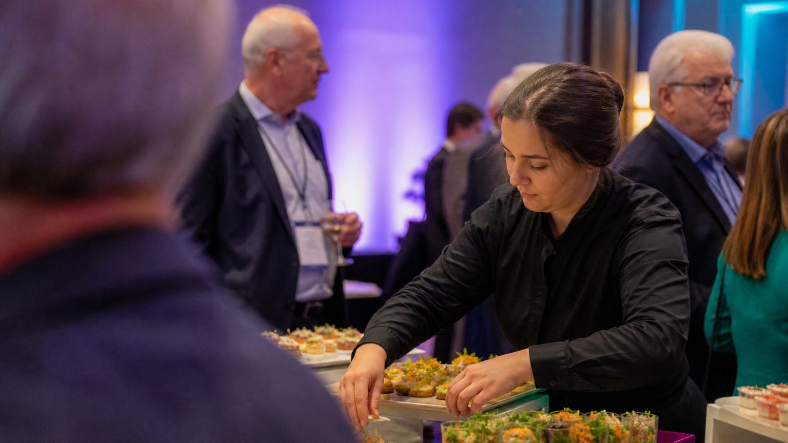 Catering staff member carefully arranging a colorful assortment of clearly labeled gluten-free, vegan, and nut-free ap