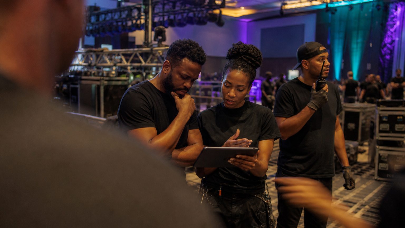 Two crew in black checking a rigging plot on a tablet while a third talks into a radio