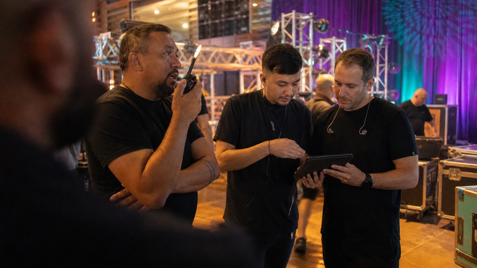 Two crew in black checking a rigging plot on a tablet while a third talks into a radio