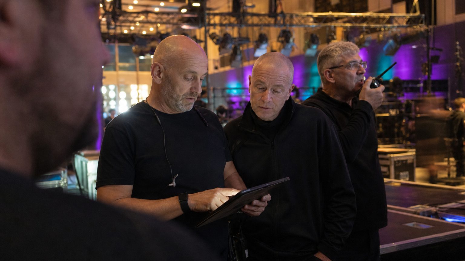 Two crew in black checking a rigging plot on a tablet while a third talks into a radio