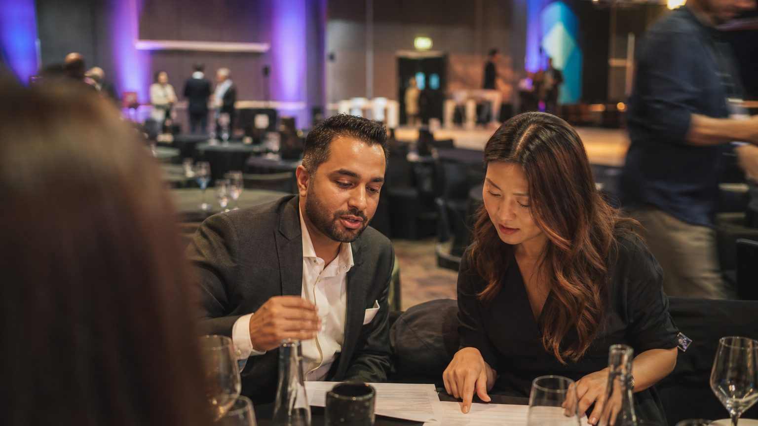 Two corporate planners reviewing printed event feedback at a table after an event