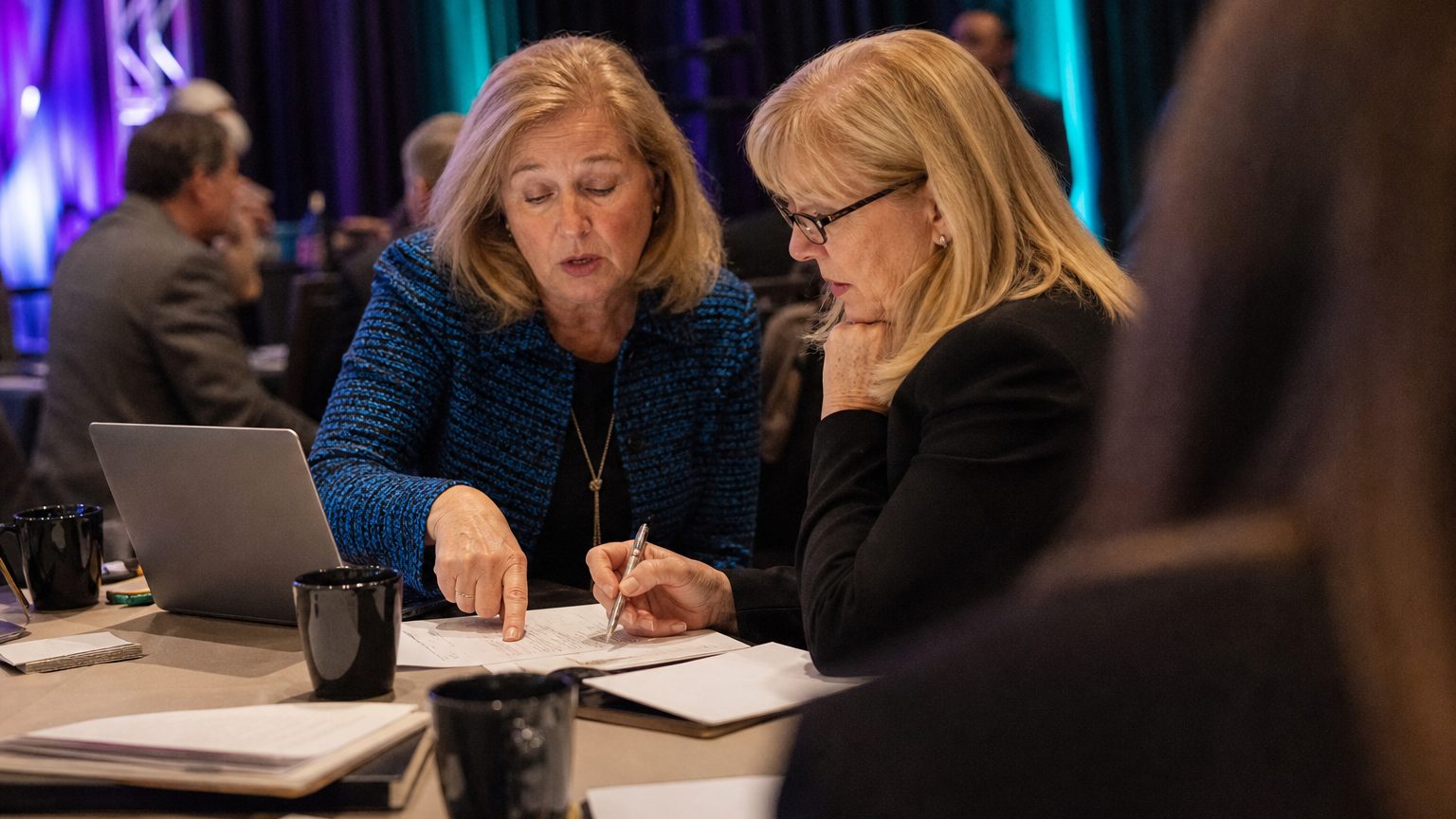 Two corporate event planners across a hotel meeting-room table mid-discussion