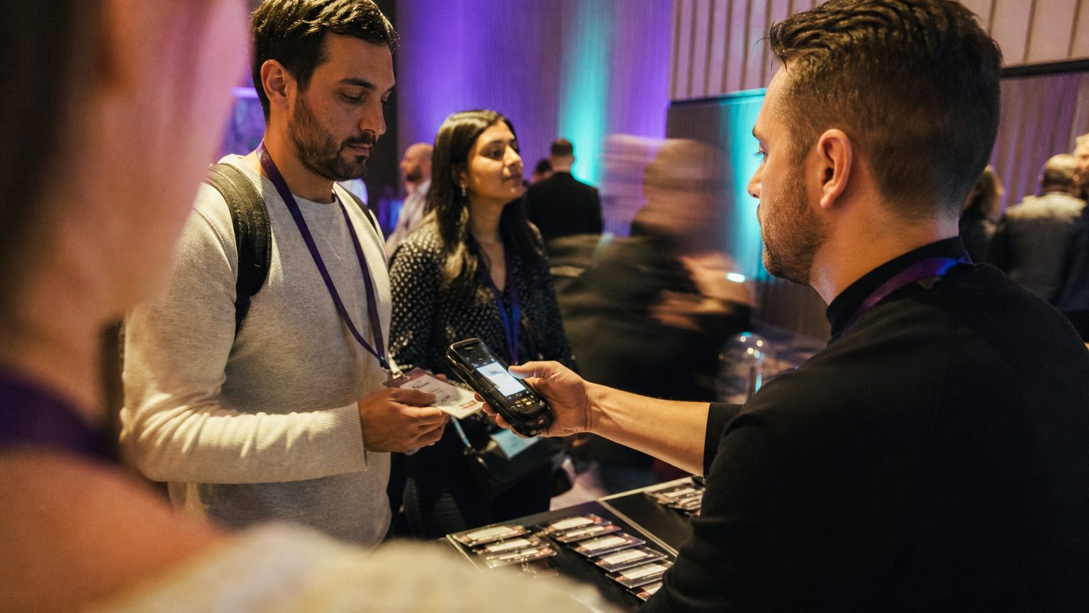 Close-up of an event staff member scanning a QR code on an attendee’s badge with a handheld device at a registration d