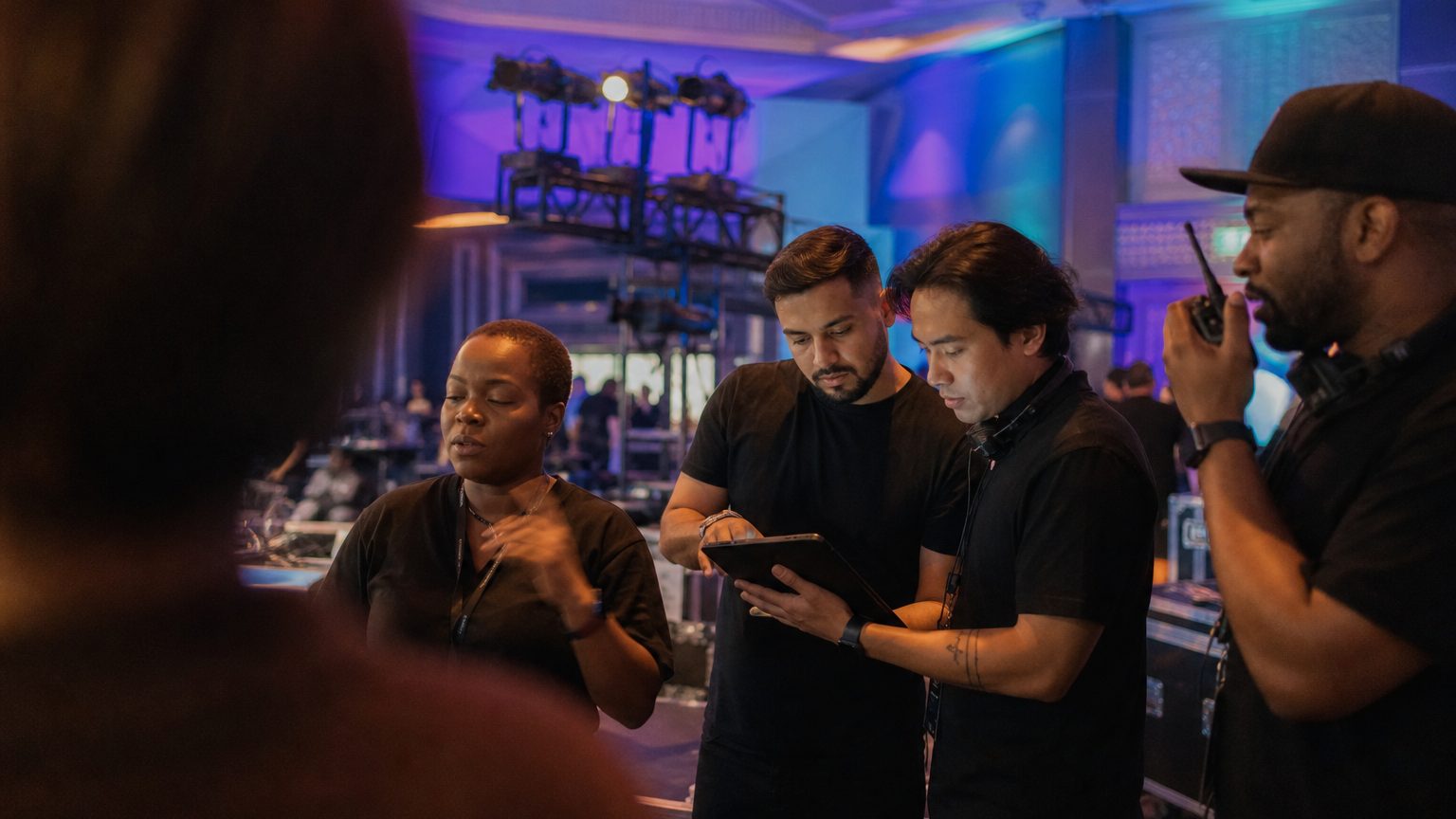 Two crew in black checking a rigging plot on a tablet while a third talks into a radio