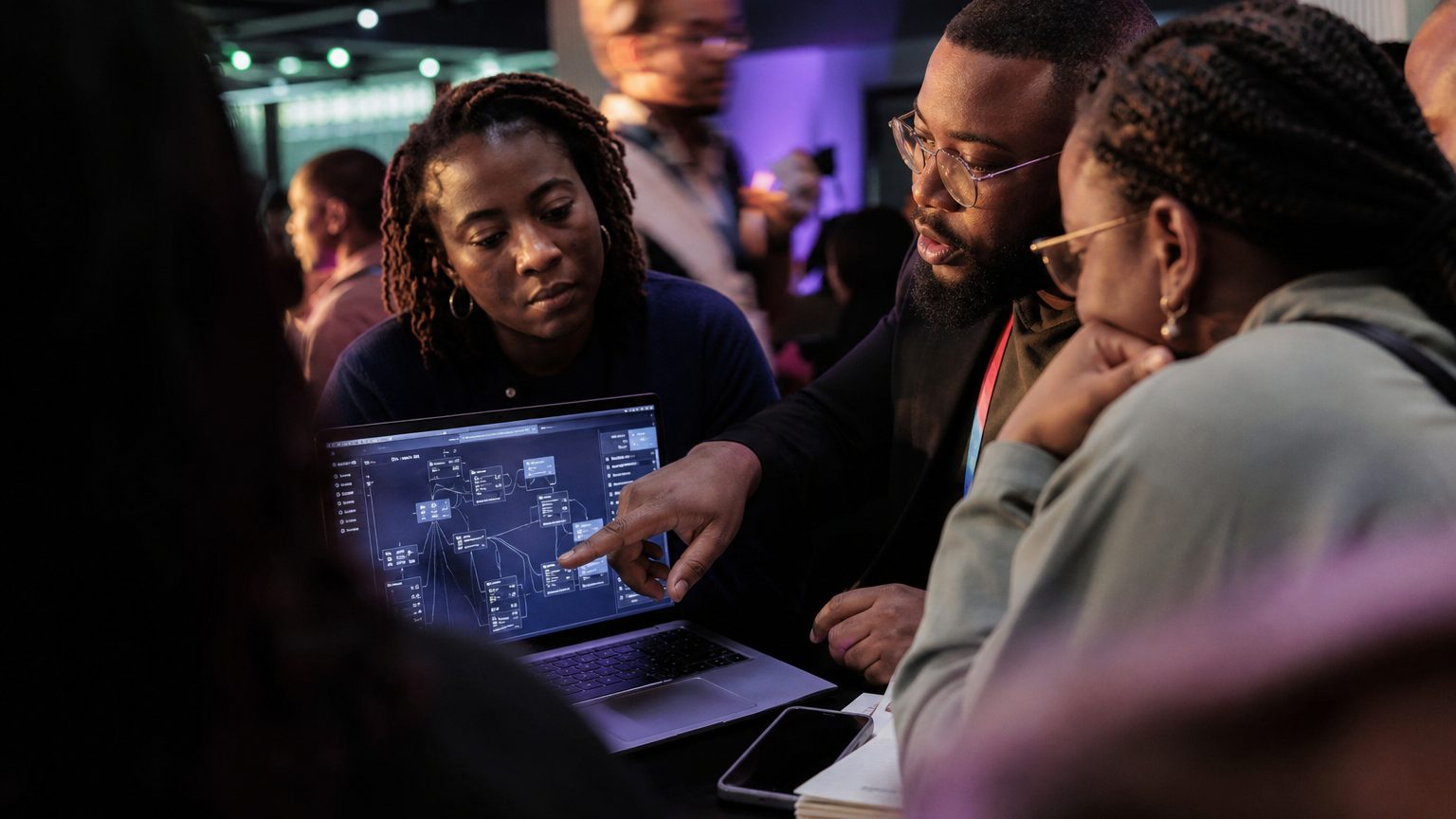 Close-up of a team gathered around a laptop screen displaying a cybersecurity software dashboard, hands pointing at da