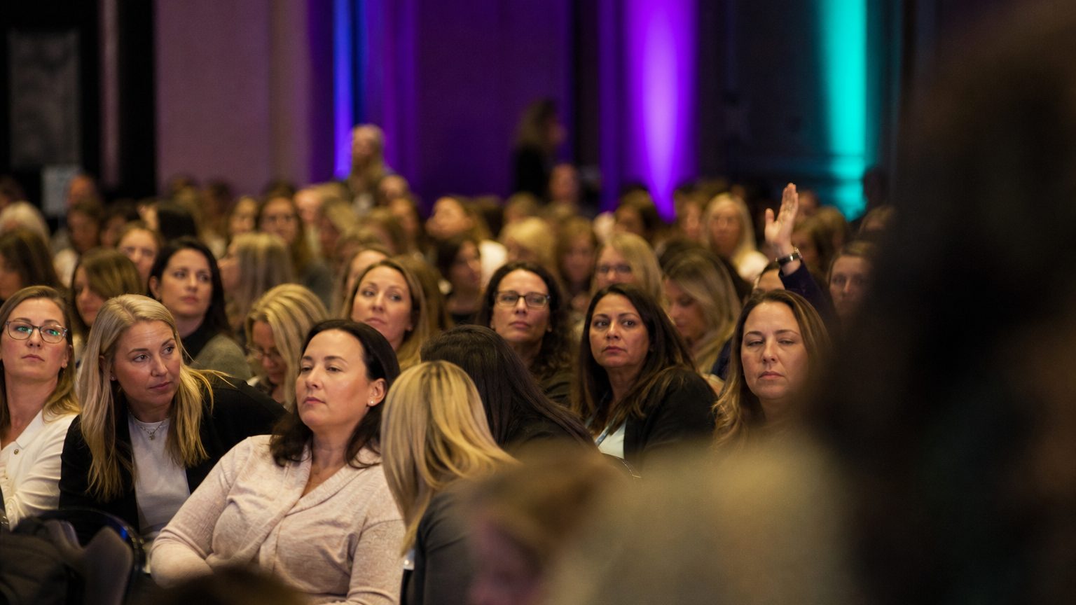 A presenter gesturing at the front of a packed ballroom