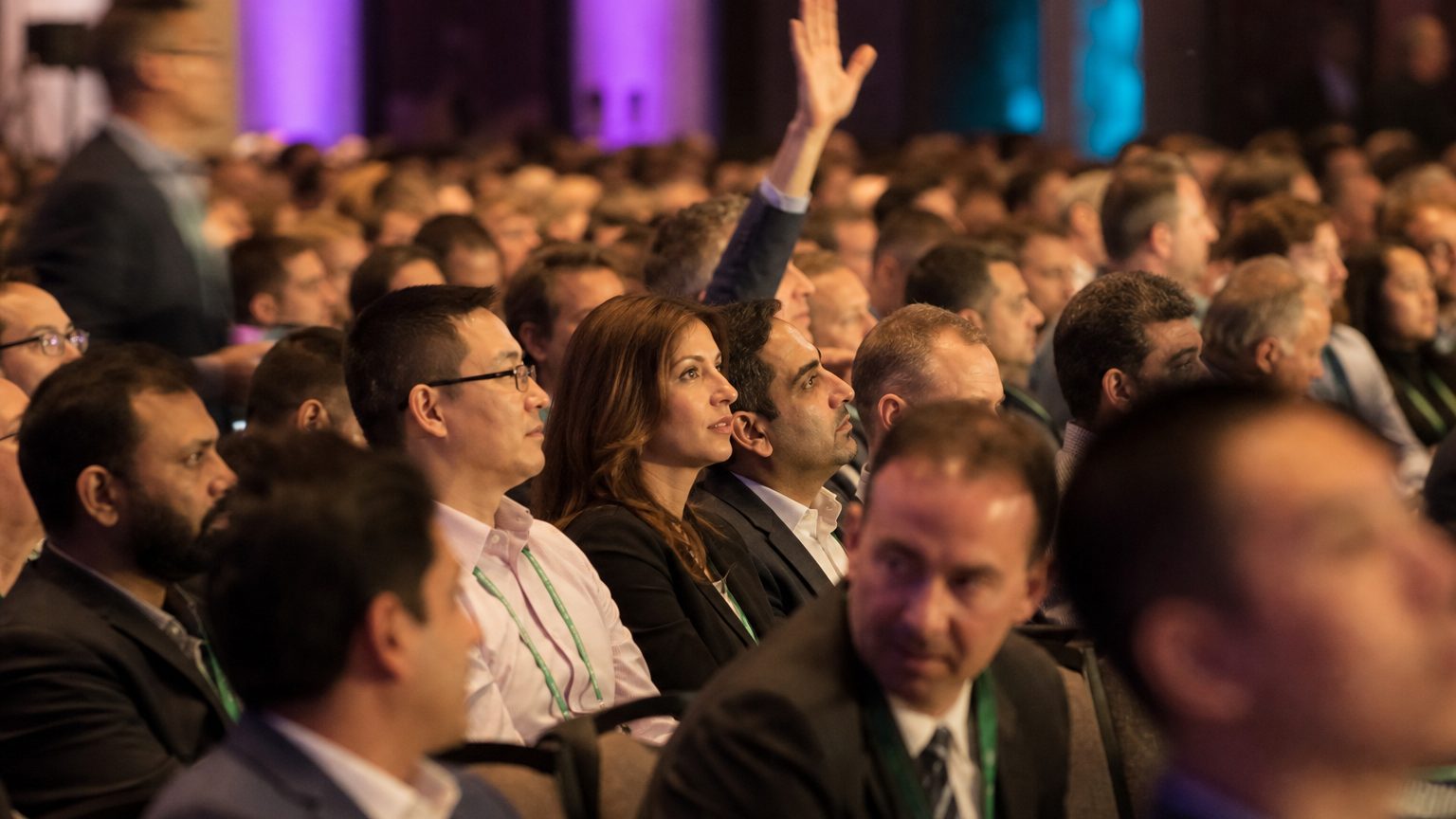 A packed sales kickoff audience with one attendee raising a hand