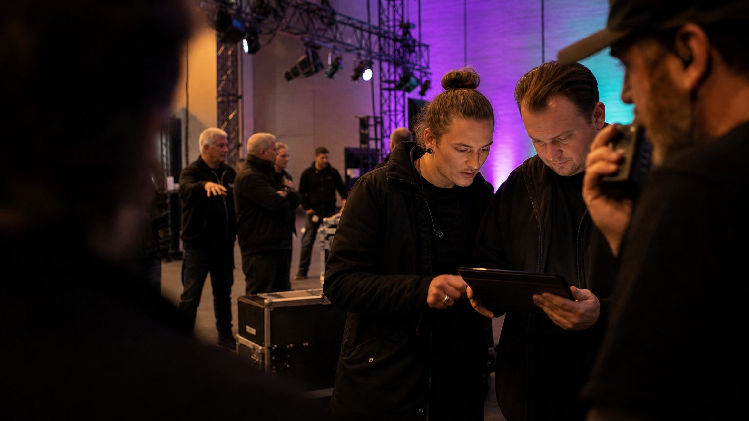 Two crew in black checking a rigging plot on a tablet while a third talks into a radio