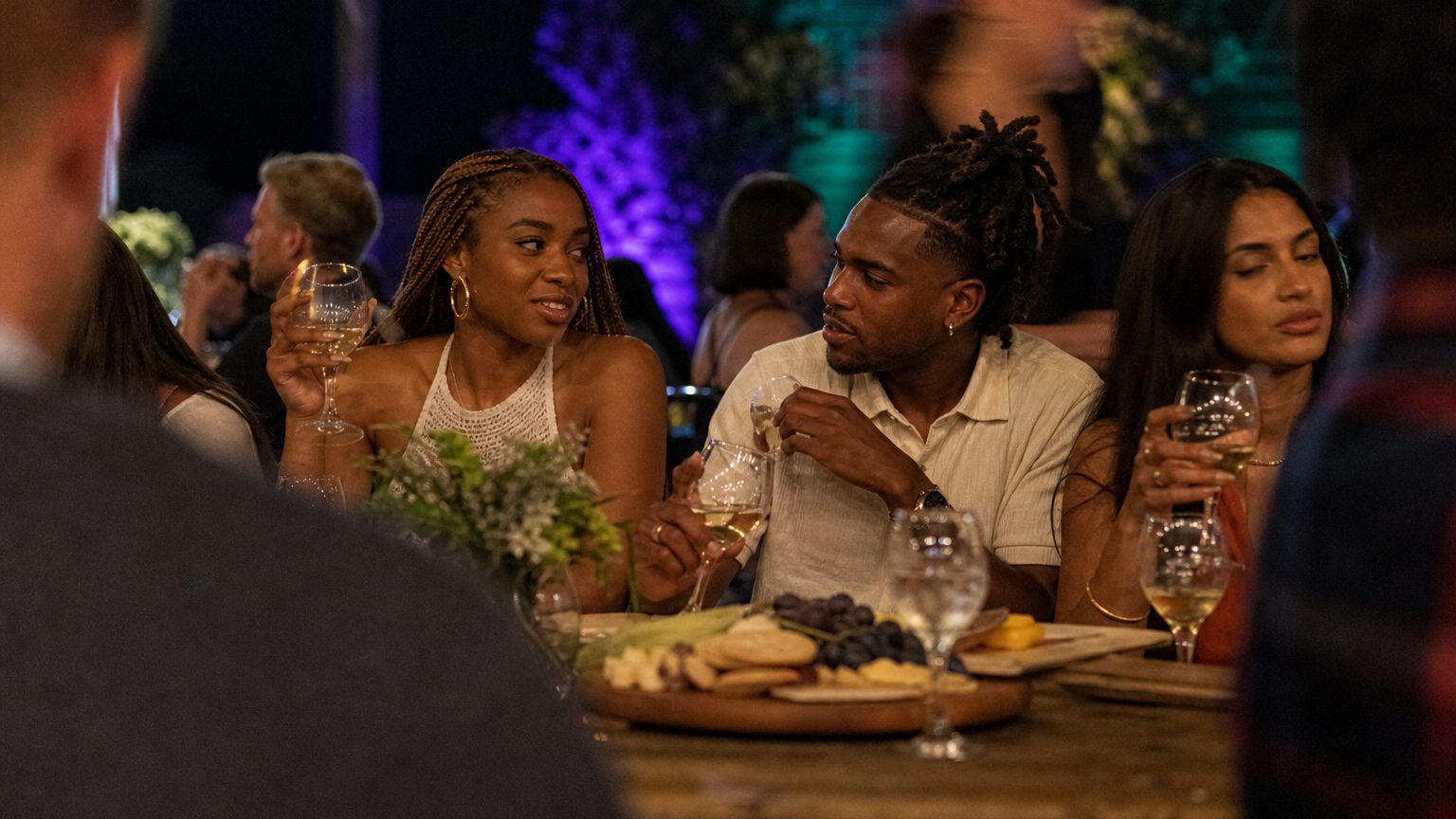 Guests enjoying a lively outdoor wine tasting event at sunset, swirling glasses and savoring flavors while seated arou