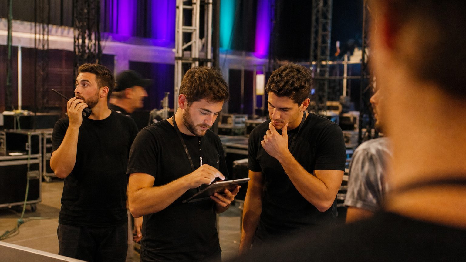 Two crew in black checking a rigging plot on a tablet while a third talks into a radio