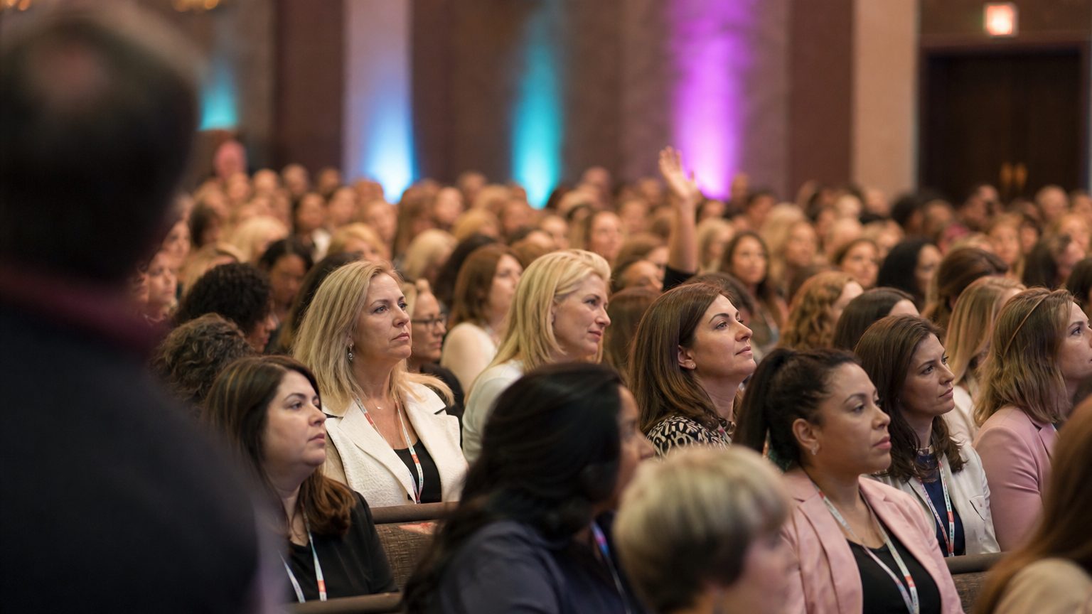 A presenter gesturing at the front of a packed ballroom