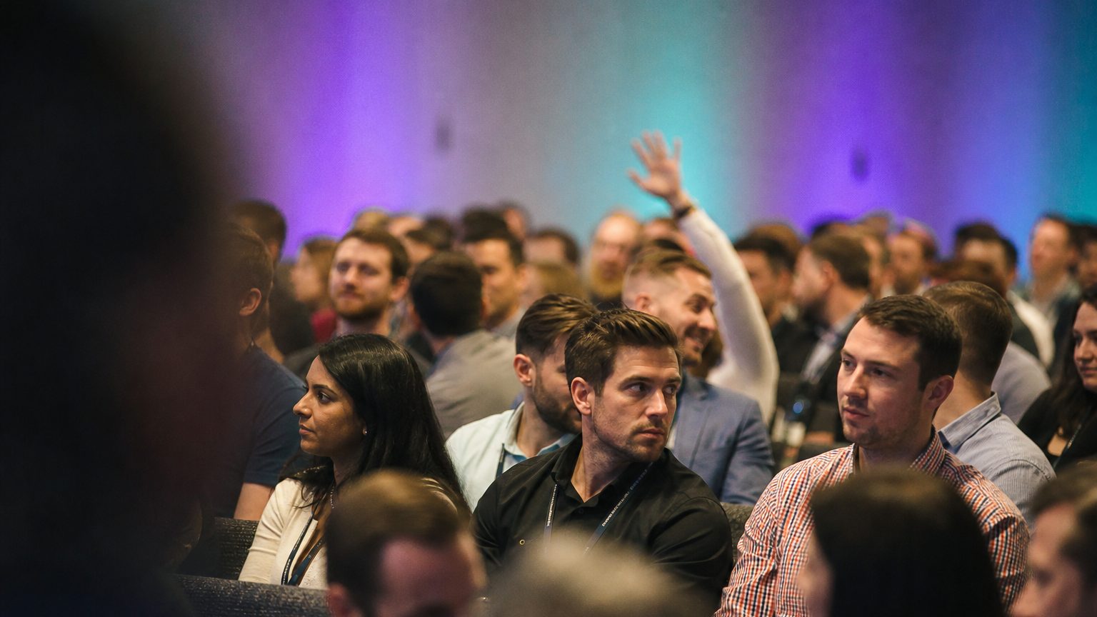 A presenter gesturing at the front of a packed ballroom