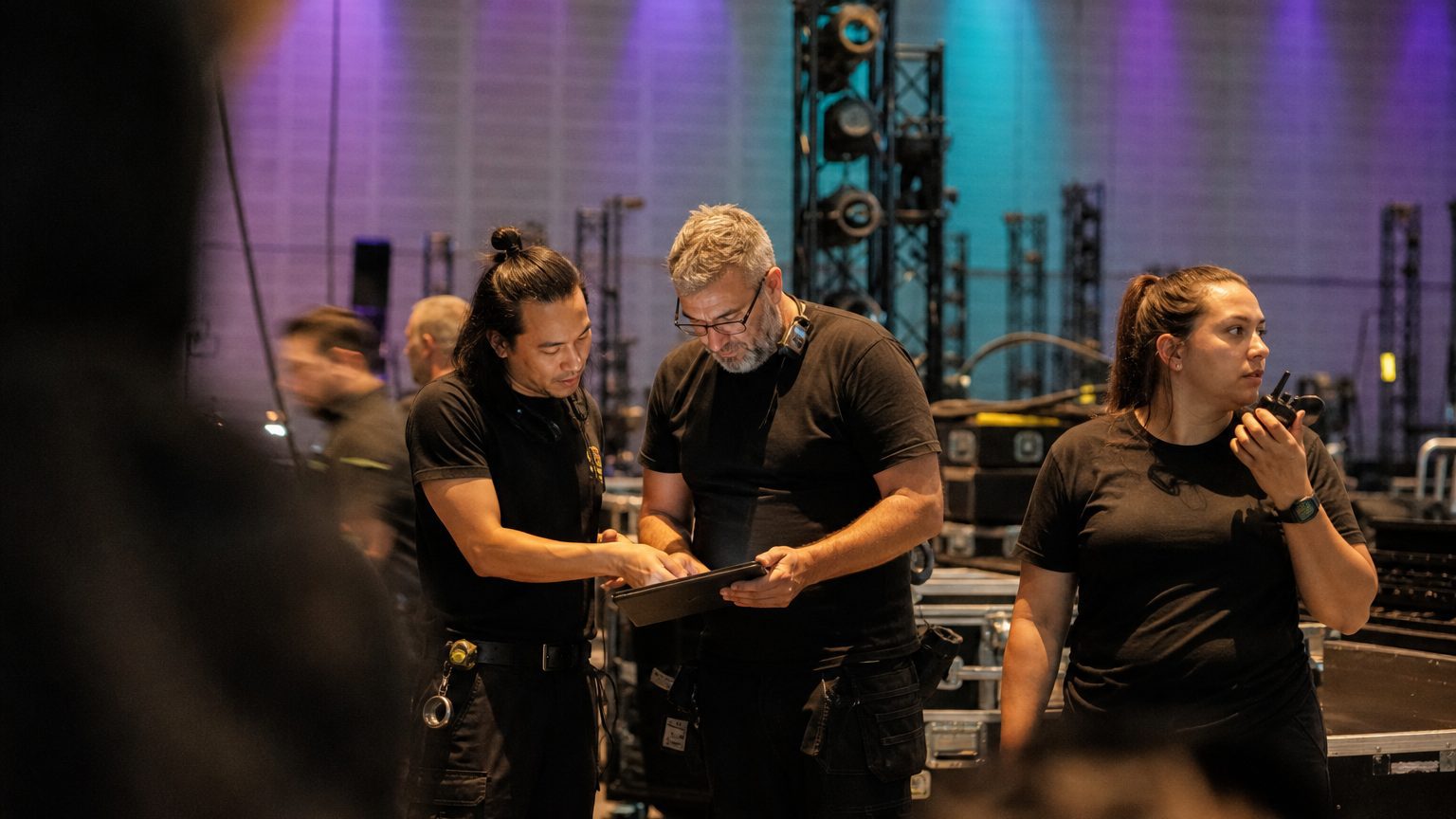 Two crew in black checking a rigging plot on a tablet while a third talks into a radio
