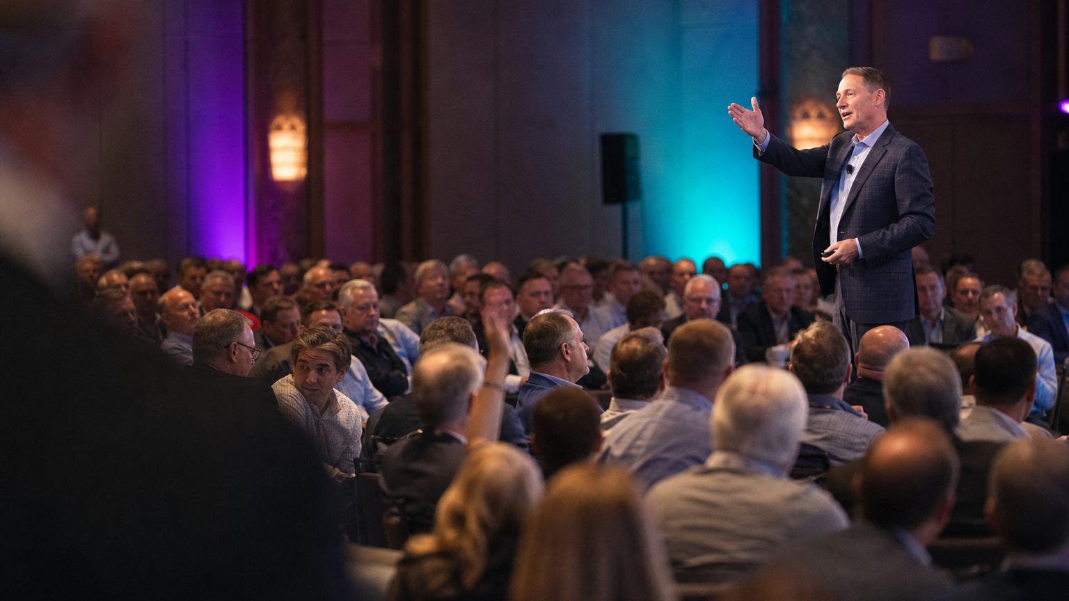 Executive presenting to a large seated sales kickoff audience under stage lighting