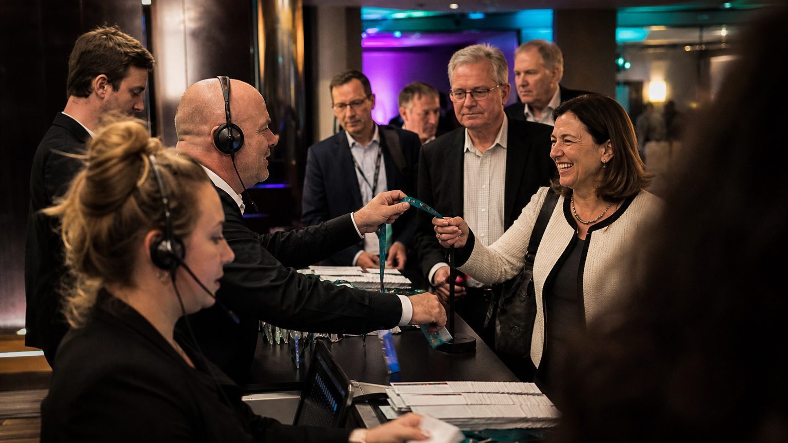 Three staff in headsets handing badges across the counter to arriving attendees