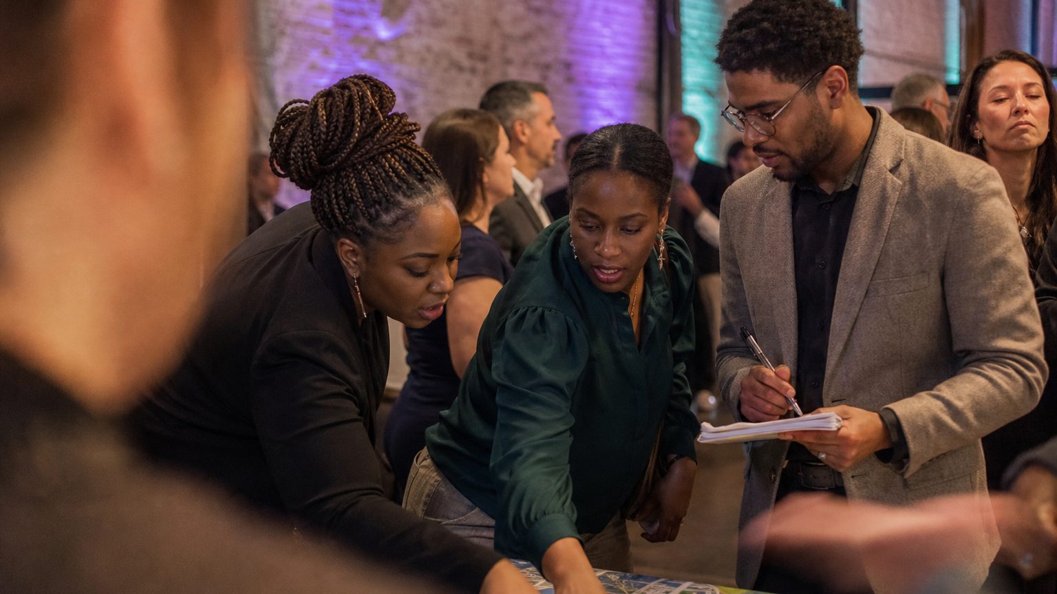 Small group of event planners crouches around a detailed city map spread on a table, one person points to a potential 