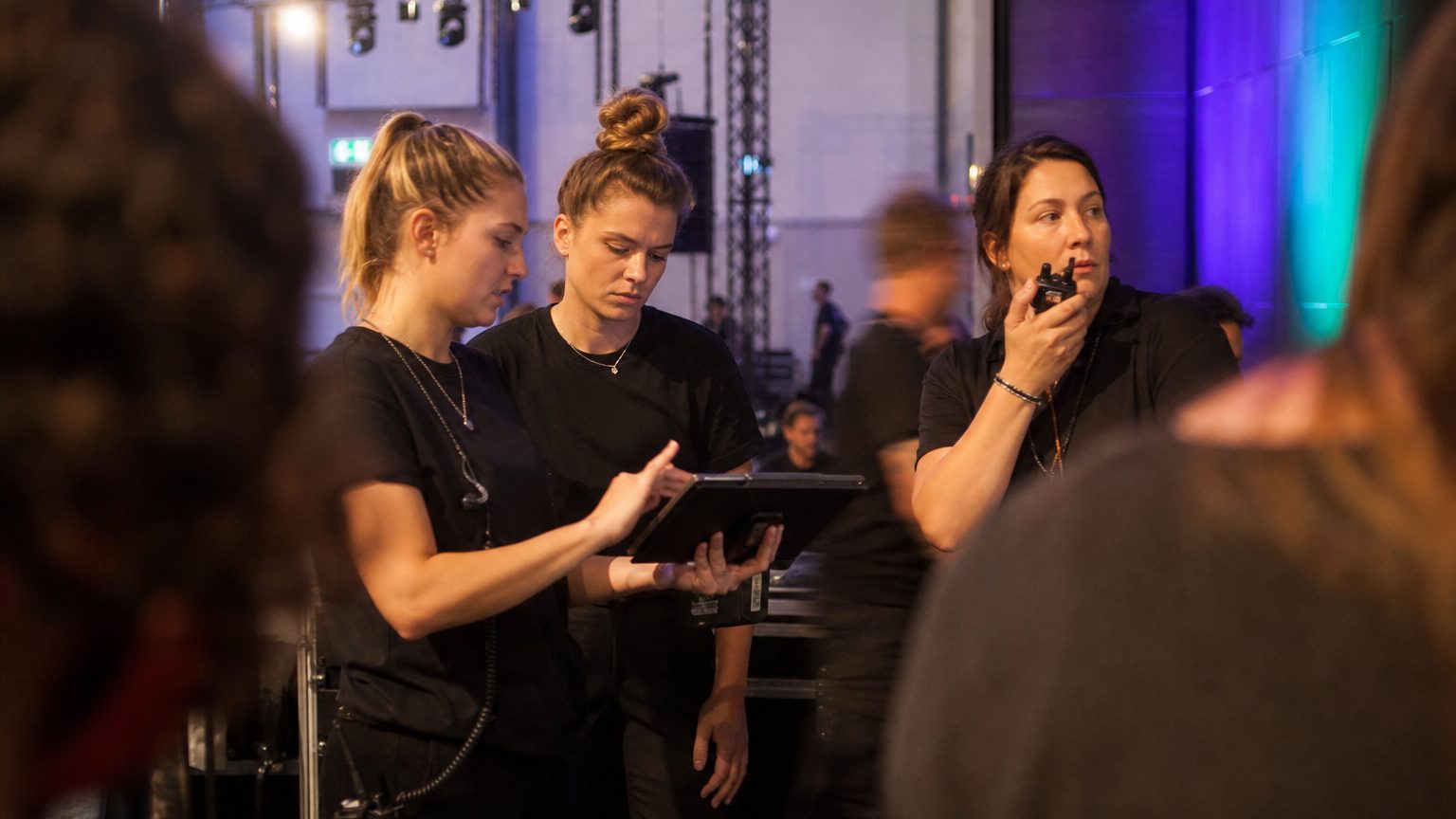 Two crew in black checking a rigging plot on a tablet while a third talks into a radio