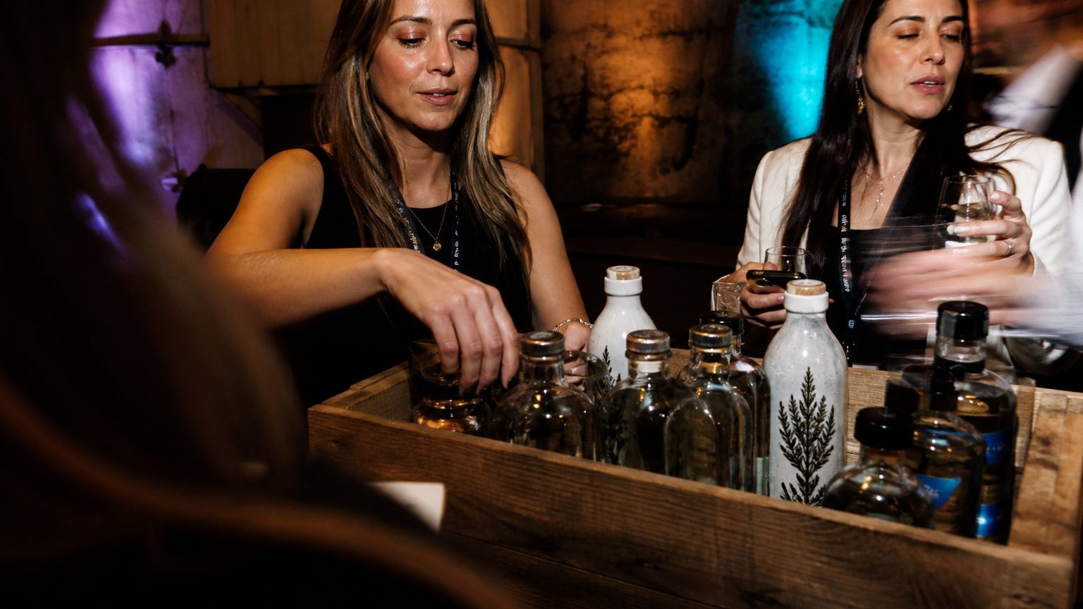 Close-up of a person’s hands carefully selecting small-batch tequila bottles from a wooden crate, with visible labels