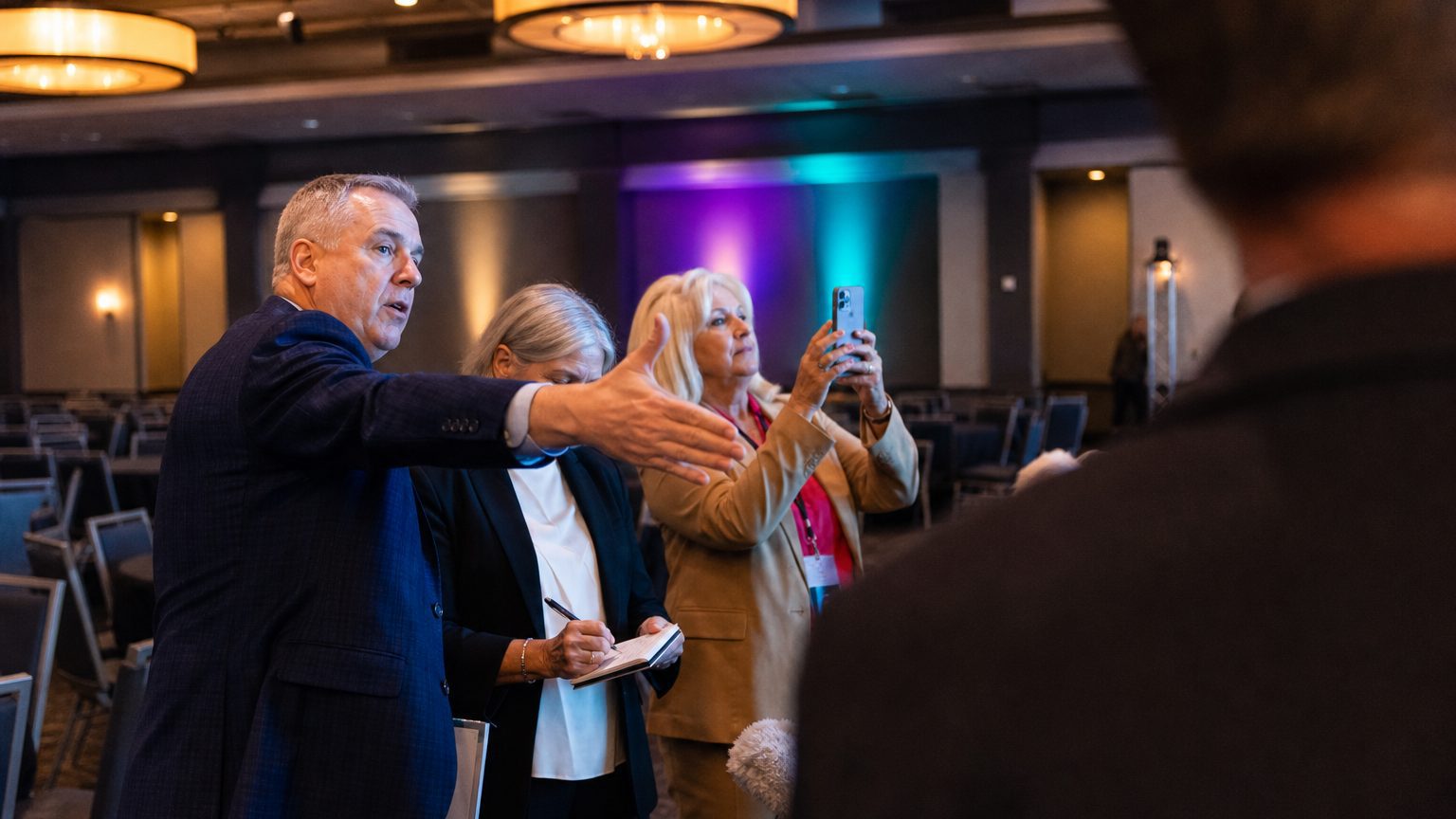 A venue manager gesturing across a function space to two corporate planners