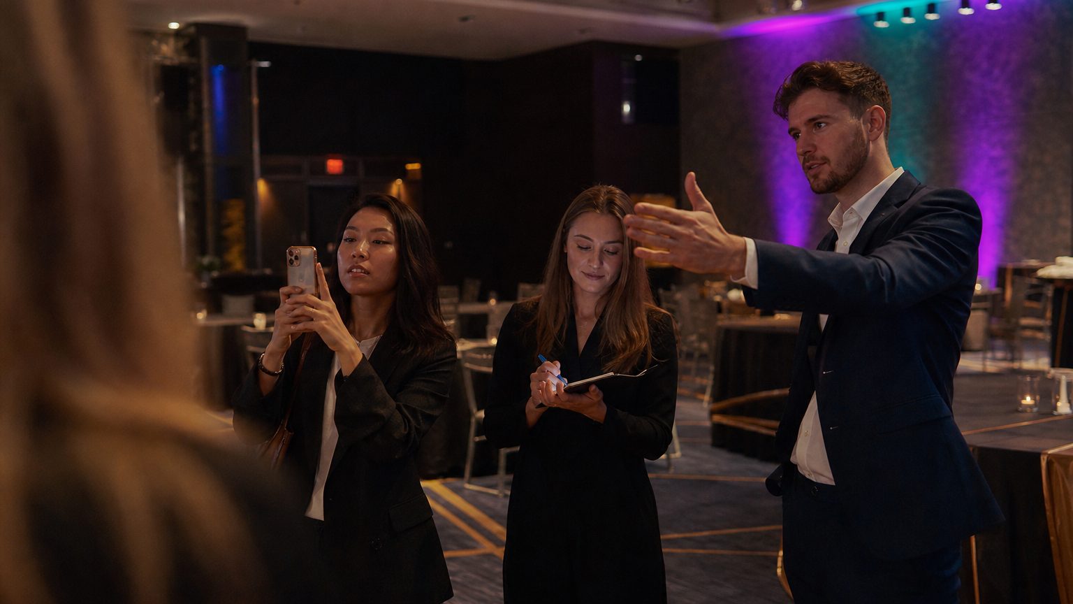 A venue manager gesturing across a function space to two corporate planners
