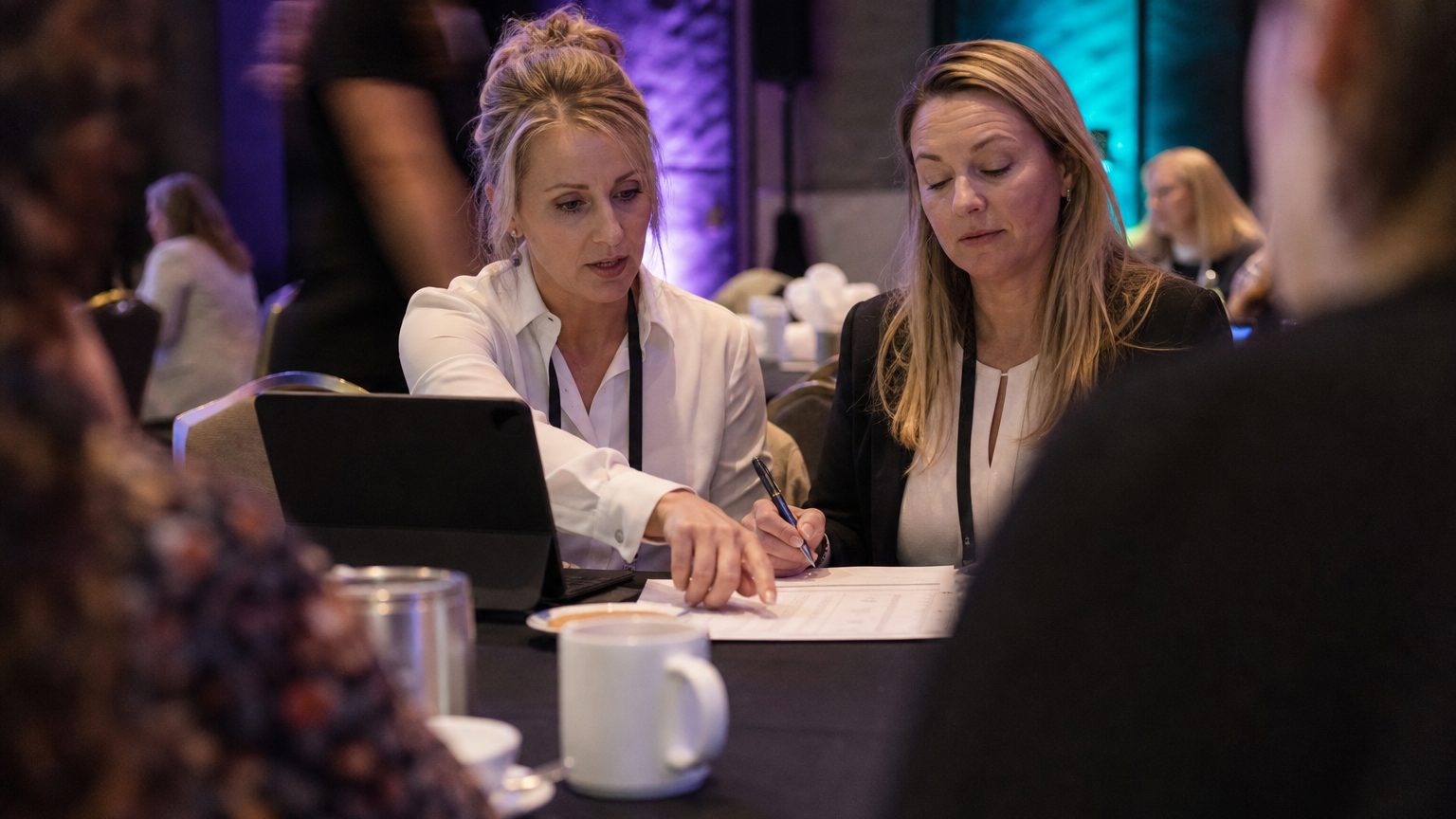 Two corporate event planners across a hotel meeting-room table mid-discussion