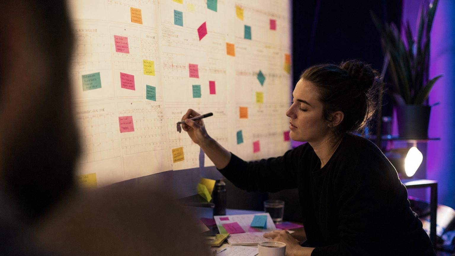 Planner sits at a desk surrounded by calendar pages and colorful sticky notes, using a pen to mark key dates and deadl