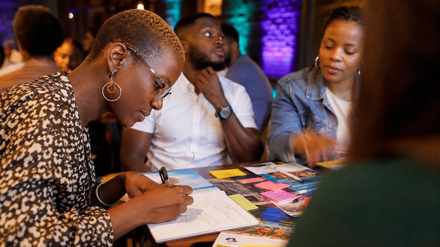 Close-up of an event planner’s hands sketching game elements and rules on a notepad, surrounded by colorful sticky not