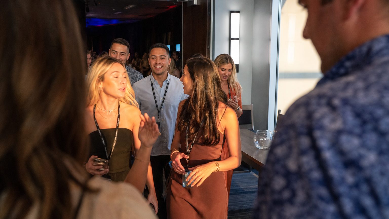 A group of incentive winners streams out of a general session through double doors into a sunlit foyer, lanyards swinging, conversations breaking open, while a registration desk nearby sits unstaffed and its feedback collection bowl sits empty.